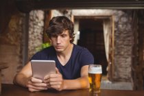 Homem usando tablet digital com copo de cerveja na mesa no bar — Fotografia de Stock