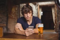 Homme utilisant un téléphone portable avec verre de bière sur la table dans le bar — Photo de stock