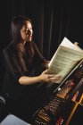 Female student looking at sheet music while playing a piano in a studio — Stock Photo