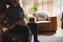 Imagen recortada de la mujer embarazada realizando ejercicio de estiramiento en la pelota de fitness en la sala de estar en casa - foto de stock