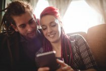 Улыбающаяся пара хипстеров с помощью мобильного телефона дома — стоковое фото
