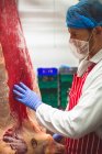 Male butcher touching red meat in storage room — Stock Photo
