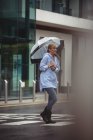Belle femme tenant parapluie et traversant la rue pendant la saison des pluies — Photo de stock