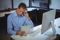 Pensativo hombre de negocios utilizando tableta digital y PC de escritorio en la oficina - foto de stock