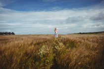 Donna con la mano nei capelli che cammina attraverso il campo di grano nella giornata di sole — Foto stock