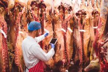 Мясник в хранилище с помощью цифрового планшета при проверке наклеек штрих-кода на мясо — стоковое фото