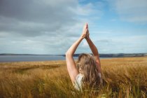 Rückansicht einer Frau mit erhobenen Händen über dem Kopf in Gebetsposition auf einem Feld an einem sonnigen Tag — Stockfoto