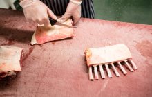 Manos de carnicero cortando costillas de cerdo en la carnicería - foto de stock