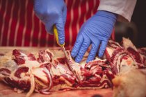 Mani di macellaio taglio di carne rossa in macelleria — Foto stock