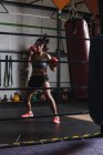Boxeadora femenina practicando boxeo con saco de boxeo en gimnasio - foto de stock