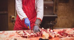 Mid section of butcher cutting red meat at butchers shop — Stock Photo