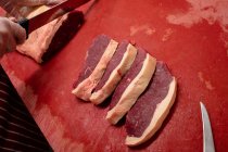 Mano de carnicero rebanando carne en carnicería - foto de stock