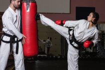 Seitenansicht von Kämpfern, die im Studio Karate mit Boxsack üben — Stockfoto