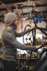 Mecánico examinando una bicicleta en taller de bicicleta - foto de stock