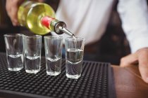 Close-up of bartender pouring tequila in shot glasses on bar counter at bar — Stock Photo