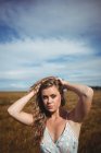Ritratto di donna con le mani nei capelli in piedi nel campo di grano nella giornata di sole — Foto stock