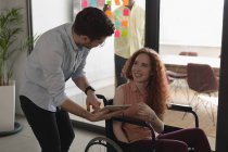 Керівник на інвалідному візку обговорює на цифровому планшеті з колегою в офісі — стокове фото