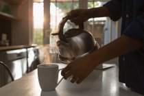 Низька частина жінки, що заповнює кухоль гарячою водою на кухні — стокове фото