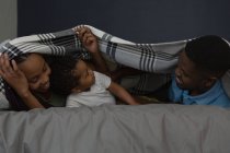 Famille couchée sous un drap de lit dans un salon à la maison — Photo de stock
