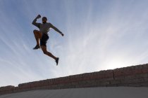 Низкий угол обзора прыжка спортсмена с окружающей стены — стоковое фото
