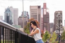 Seitenansicht einer Frau, die sich an einem sonnigen Tag an ein Geländer lehnt — Stockfoto
