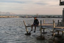 Male athlete sitting on pier at beach — Stock Photo