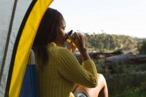 Woman having coffee near tent in the forest — Stock Photo