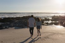 Вид сзади на пару, держащуюся за руки и идущую по пляжу — стоковое фото