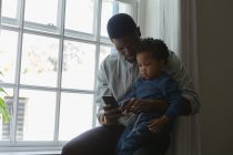 Father showing son a mobile phone in a living room at home — Stock Photo