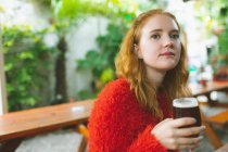 Рыжая женщина держит стакан пива в кафе на открытом воздухе — стоковое фото