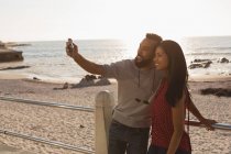 Pareja feliz tomando selfie en el teléfono móvil en el paseo marítimo - foto de stock