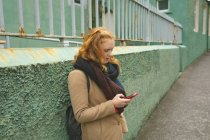 Рыжая женщина использует мобильный телефон в переулке — стоковое фото