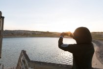 Male athlete clicking photo with mobile phone on pier — Stock Photo