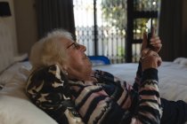 Seniorin benutzte Handy auf Bett im heimischen Schlafzimmer — Stockfoto