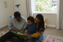 Родители читают книжку с картинками со своим сыном в гостиной дома — стоковое фото