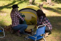 Visão traseira de mulheres colocando uma tenda na floresta — Fotografia de Stock