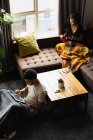 Couple utilisant téléphone portable et tablette numérique tout en prenant un café dans le salon à la maison — Photo de stock