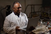 Operaio maschile che utilizza laptop in fabbrica di vetro — Foto stock