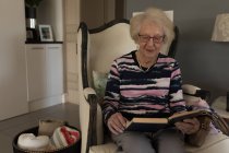 Старша жінка читає книгу у вітальні вдома — стокове фото