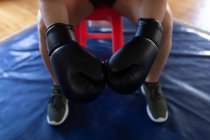 Mid section of female boxer sitting with boxing gloves in fitness studio — Stock Photo