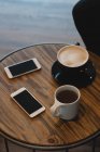 Taza de café y teléfono móvil en la mesa en la cafetería - foto de stock