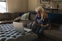 Großmutter und Enkelin machen Videoanruf auf Laptop im heimischen Wohnzimmer — Stockfoto