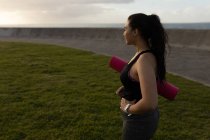 Side view of female jogger holding exercise mat in the park — Stock Photo