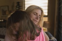 Primer plano de la madre abrazando a su hija en casa - foto de stock