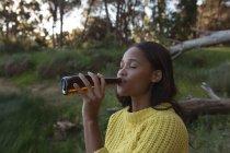 Jovem mulher bebendo cerveja na floresta — Fotografia de Stock