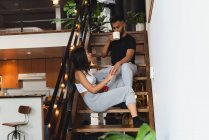 Casal interagindo uns com os outros enquanto toma café nas escadas em casa — Fotografia de Stock
