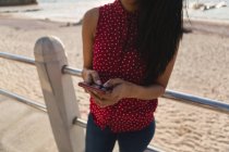 Sección media de la mujer usando el teléfono móvil en el paseo marítimo - foto de stock