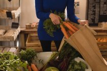 Sección media de la mujer poniendo verduras en la bolsa de la compra en el supermercado - foto de stock