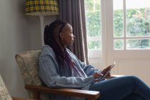 Mujer reflexiva usando tableta digital en una sala de estar en casa - foto de stock