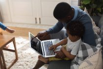 Padre e hijo usando portátil en una sala de estar en casa - foto de stock